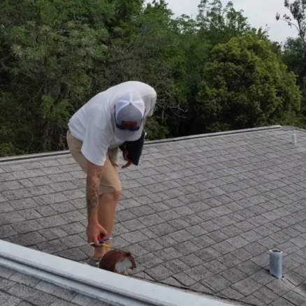 Technician measuring roof vent opening with tape measure during a detailed roof inspection to verify proper attic ventilation.